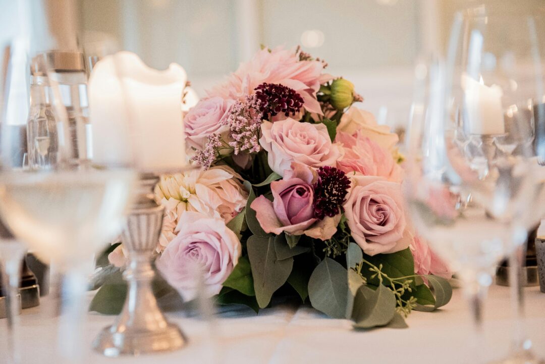 Burgundy and blush wedding centerpiece with deep wine roses, soft blush peonies, dusty rose ranunculus, and cream linen in warm candlelight at an autu