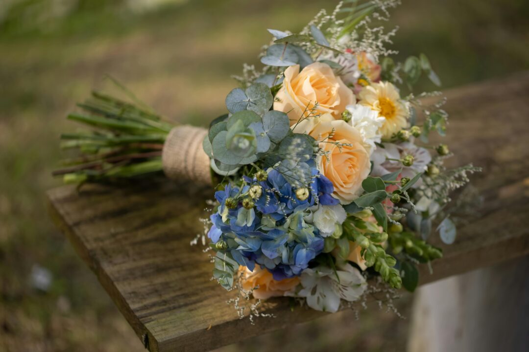 Dusty blue wedding ceremony setup with soft misty blue florals, silver-grey ribbon draping, and ivory garden roses in dappled afternoon light