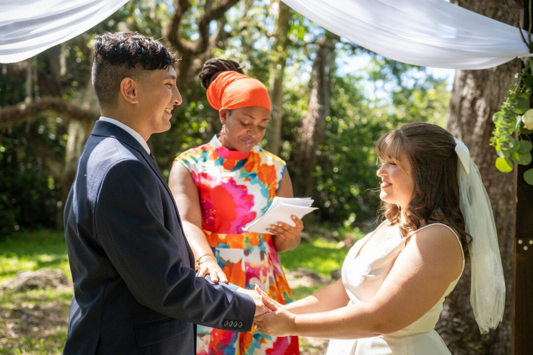 couple exchanging vows at a civil or outdoor ceremony with no religious iconography, officiant holding ceremony script, intimate and joyful atmosphere