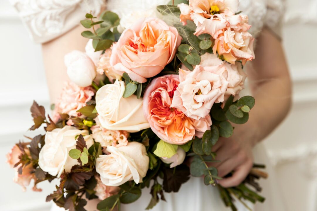 Coral and ivory wedding reception with peach and orange florals, tropical greenery, warm candlelight, and champagne linen at an outdoor summer celebra