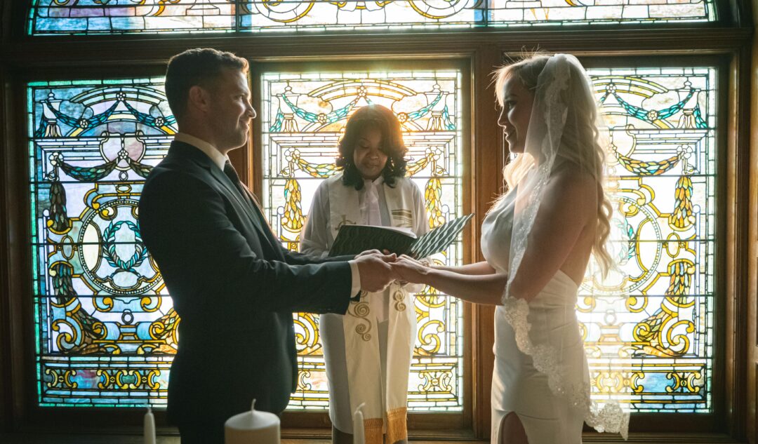 couple exchanging traditional vows in a church or chapel, stained glass light, formal attire, solemn and joyful ceremony moment, officiant presiding