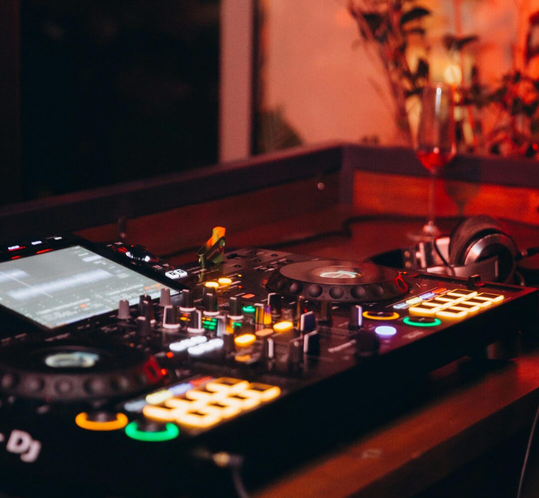 wedding DJ behind a lit console with colorful uplighting filling the reception hall, guests mid-dance in background