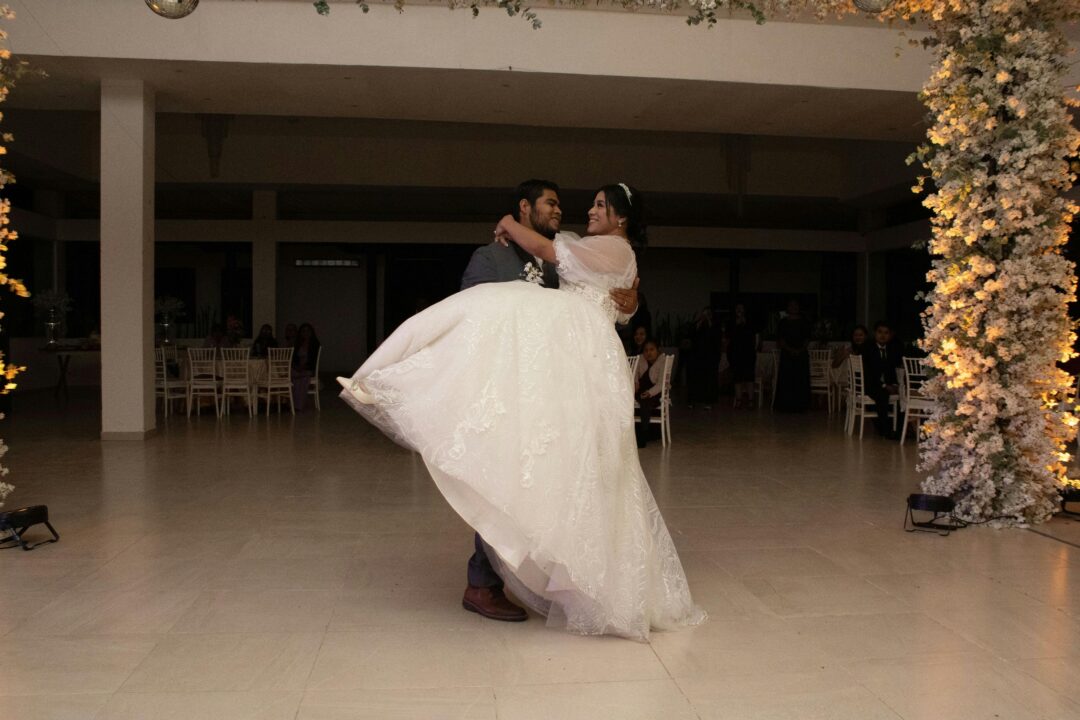wedding videographer filming a couple's first dance in a warmly lit ballroom, camera mounted on a shoulder rig with soft bokeh background