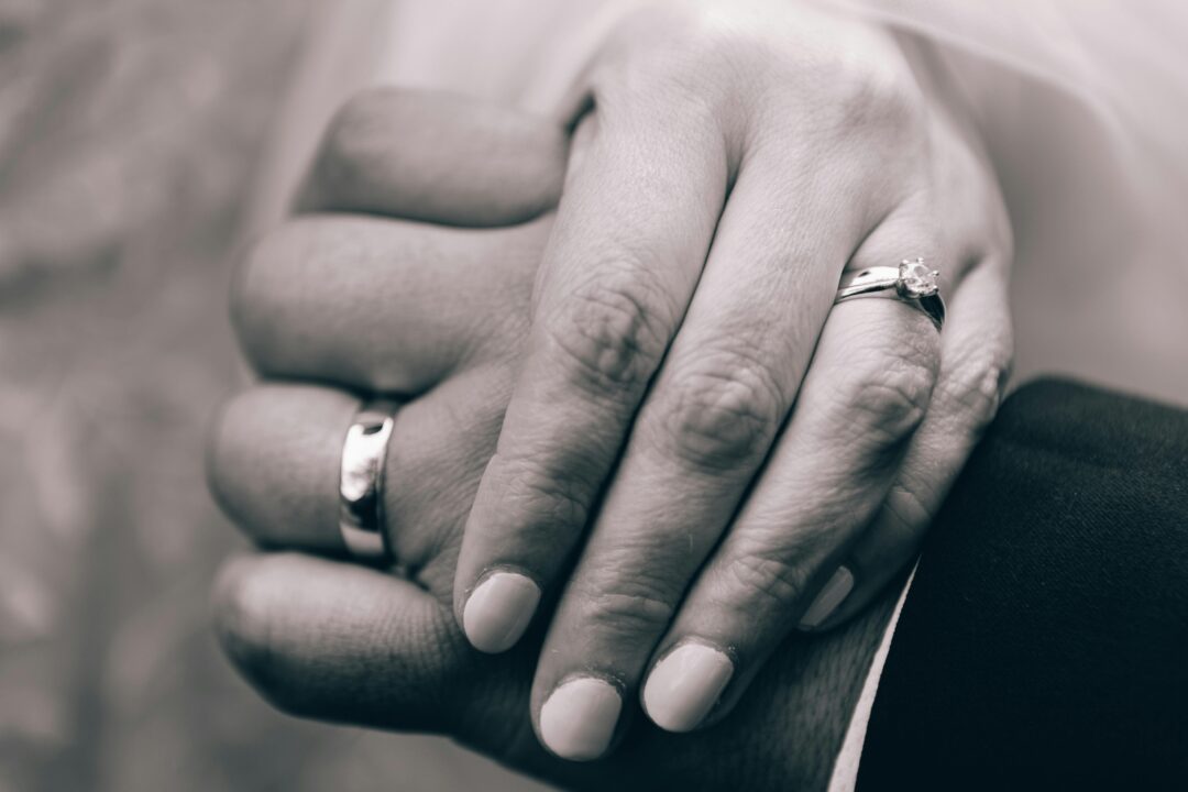 close-up of a couple's hands intertwined on a dance floor, wedding rings visible, soft warm lighting from below