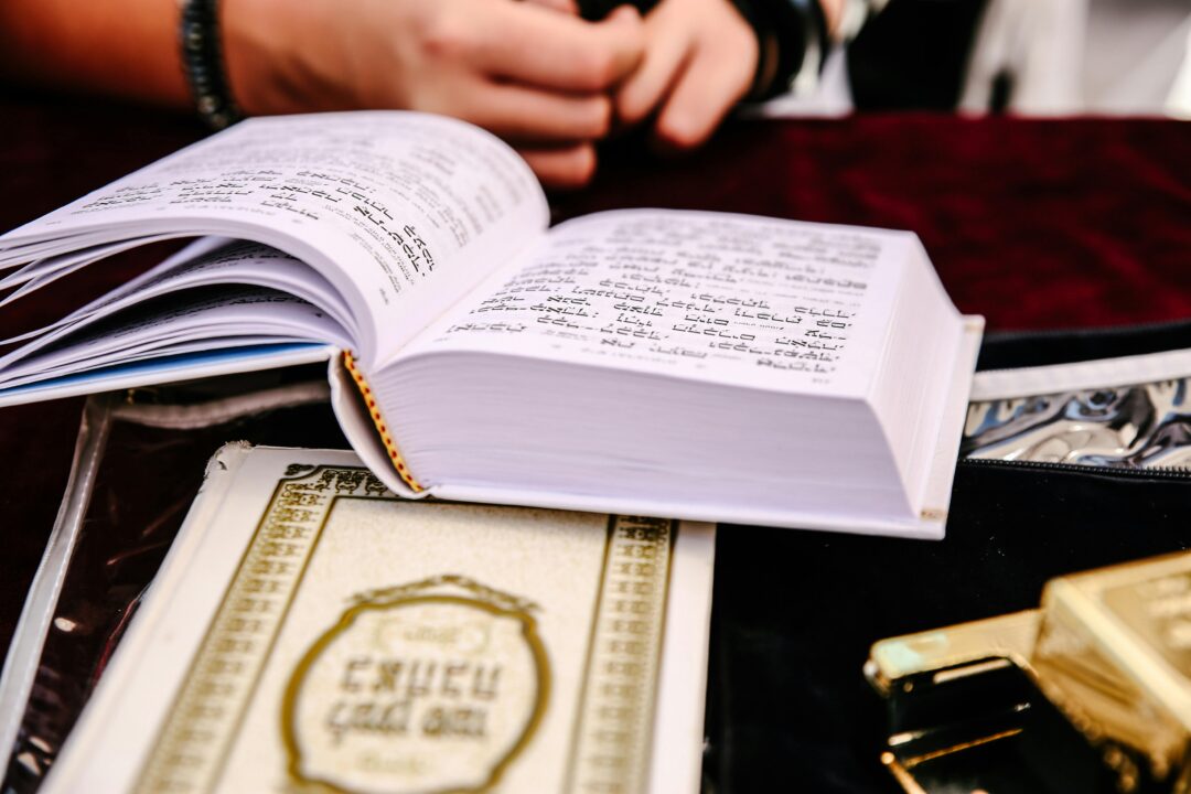 open prayer book or ketubah document resting on a decorated ceremony table, soft focus background with floral arrangements, warm ceremonial lighting