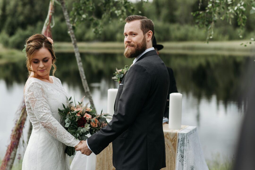 bride and groom face to face holding hands on an outdoor wedding ceremony stage, floral arch in background, warm afternoon light, candid emotional mom