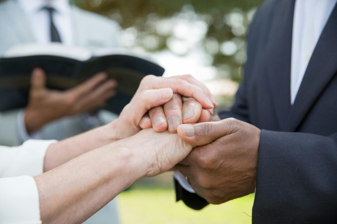 couple standing together outdoors at a ceremony, holding hands and facing each other, no altar or religious symbols visible, soft afternoon light filt
