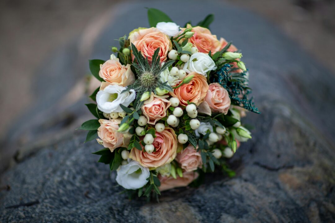 Coral and peach bridal bouquet with coral garden roses, peach ranunculus, sage greenery, eucalyptus, and cream sweet peas in a lush, round bridal gath