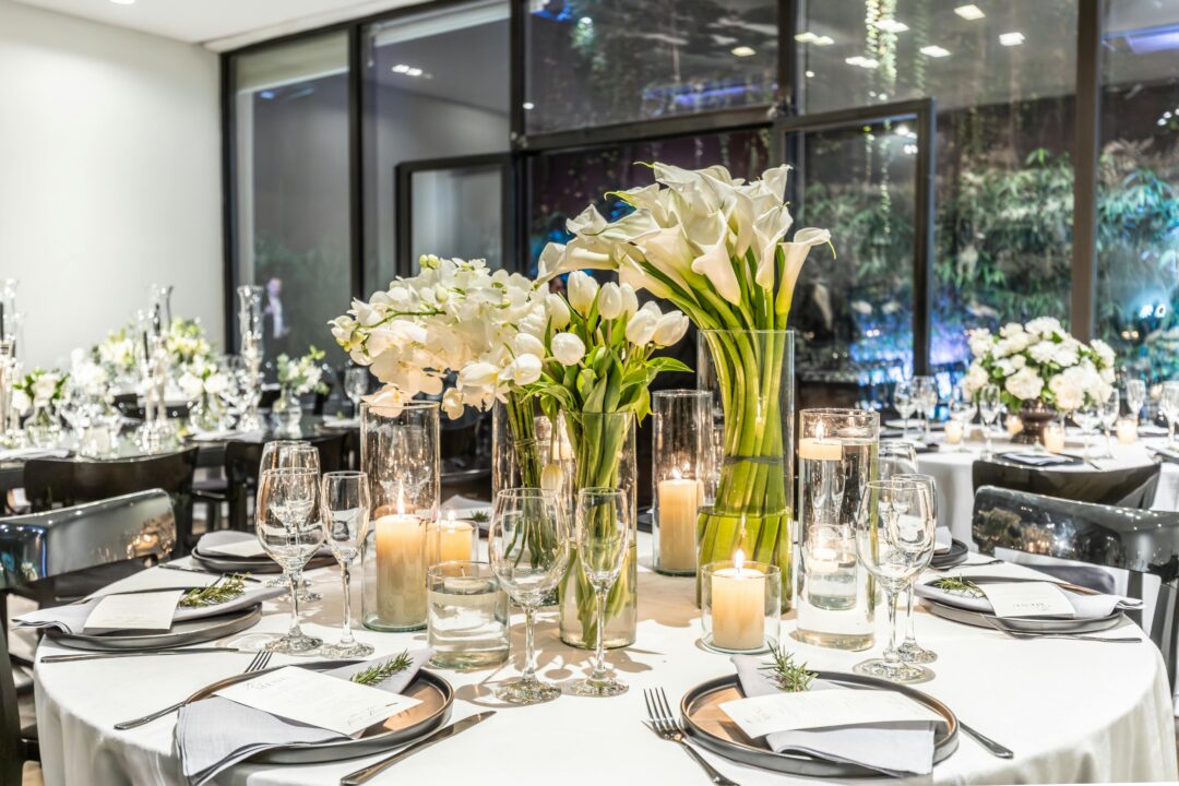 elegant wedding reception tablescape with tall floral centerpiece of white roses and greenery on a linen-covered table