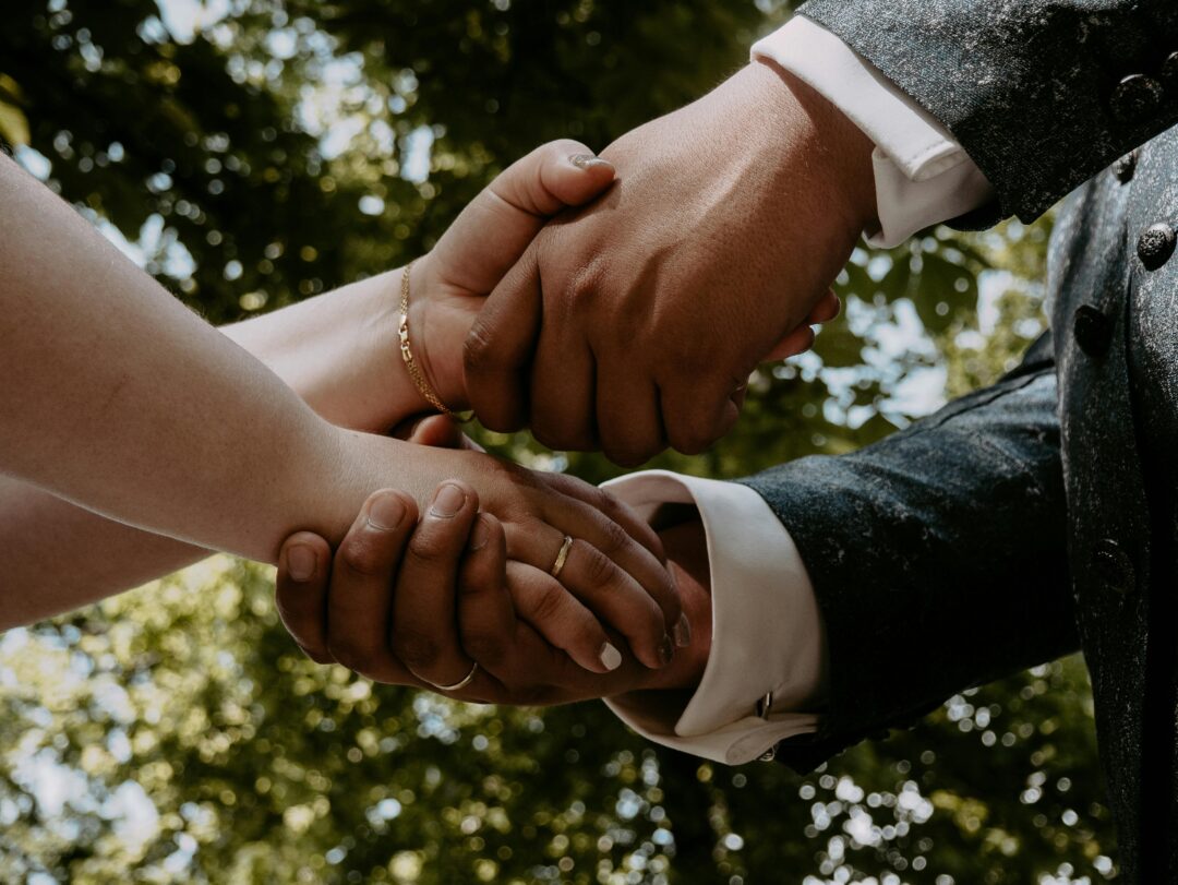 close-up of couple’s hands clasped together during vow exchange, wedding bands being placed, soft shallow depth of field, warm neutral backgroun