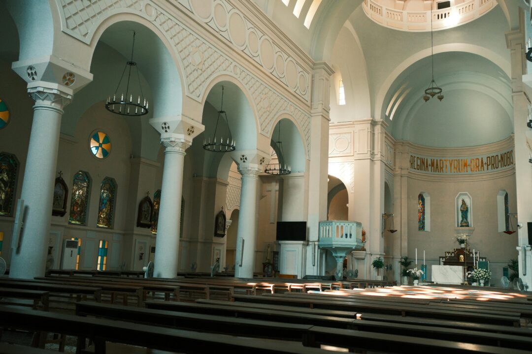 Catholic church interior with floral arch over the altar, white rose petal aisle, soft candle and stained glass light, empty ceremony setup ready for 
