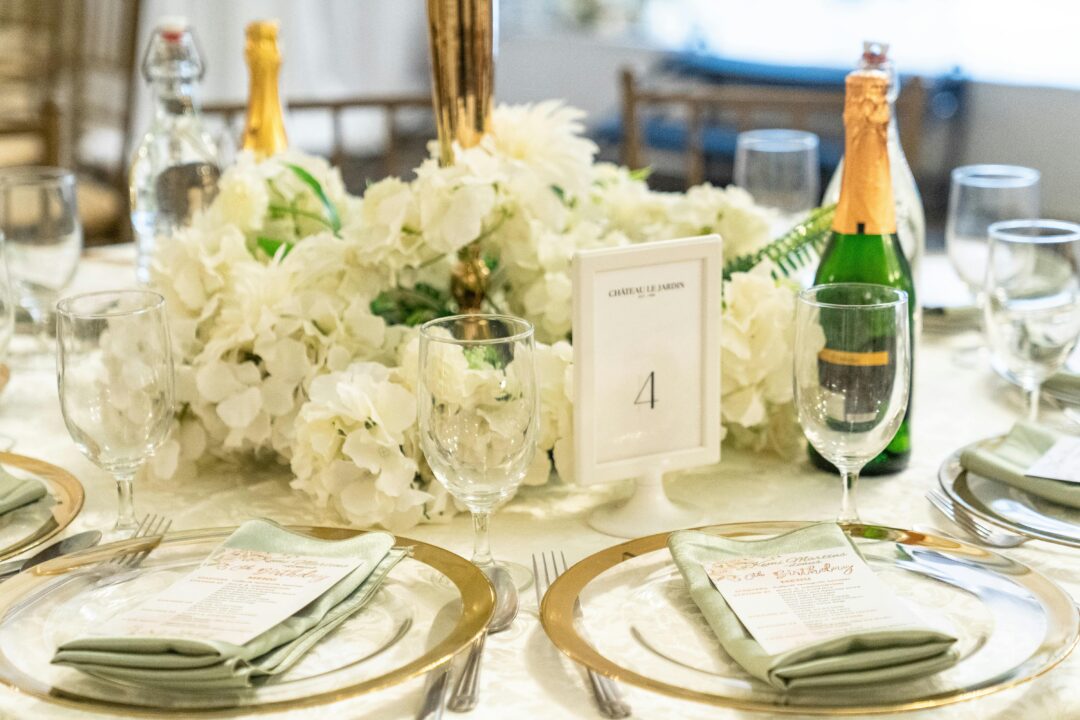 Tall navy and gold wedding centerpiece in gold cylinder vase with white garden roses, blue hydrangea, eucalyptus, and gold botanical accents on white 