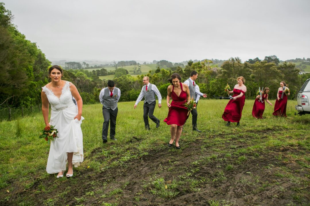 Bridesmaids in sage chiffon gowns holding deep burgundy and ivory bouquets of garden roses and eucalyptus at outdoor wedding ceremony