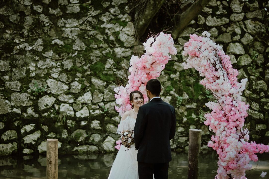 wedding ceremony musician playing acoustic guitar outdoors under a floral arch, soft afternoon light