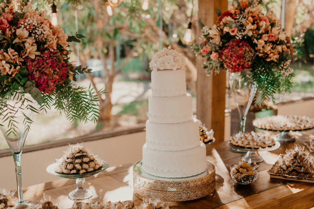 Four-tier sage green buttercream wedding cake with fresh burgundy garden roses and dried botanicals on a marble cake stand