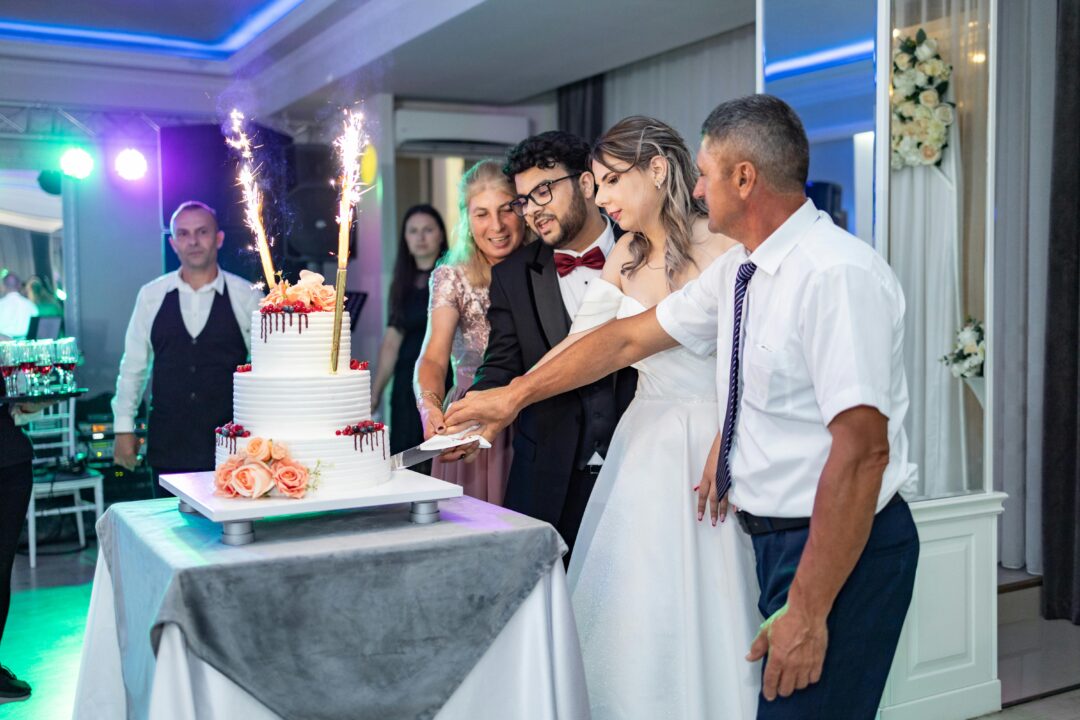 wedding guests cheering and clapping as the couple cuts the cake, champagne flutes visible, festive atmosphere