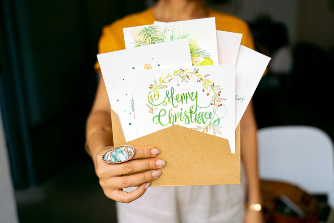 Stack of finished Christmas cards in red letterbox or postal tray ready to send, festive but minimal styling, daylight editorial flat-lay