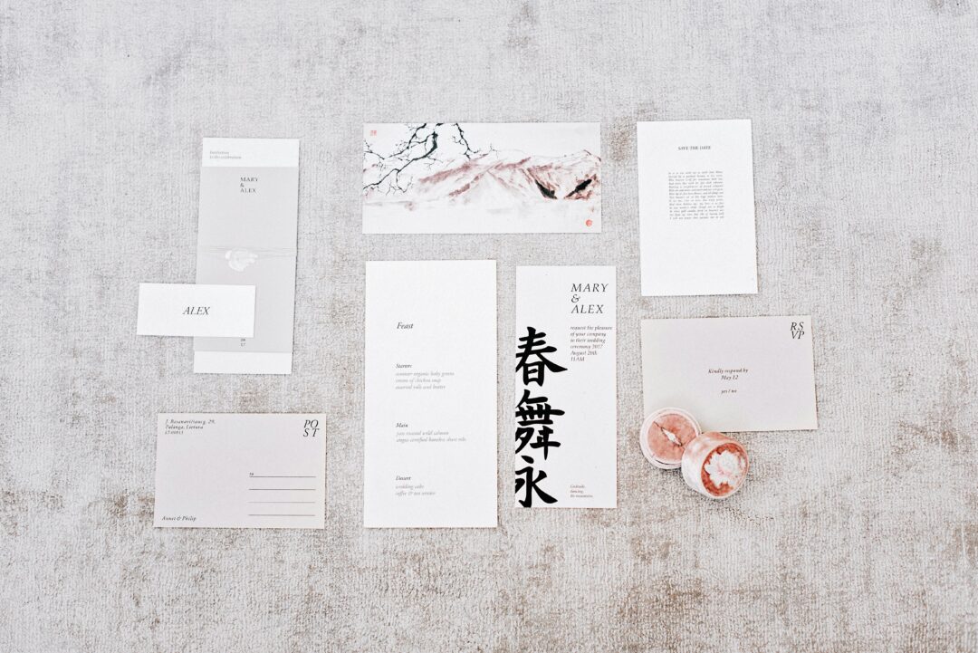 wedding stationery flat-lay including printed menu cards, place cards with dietary symbols, and a folded seating chart on a wooden table with eucalypt
