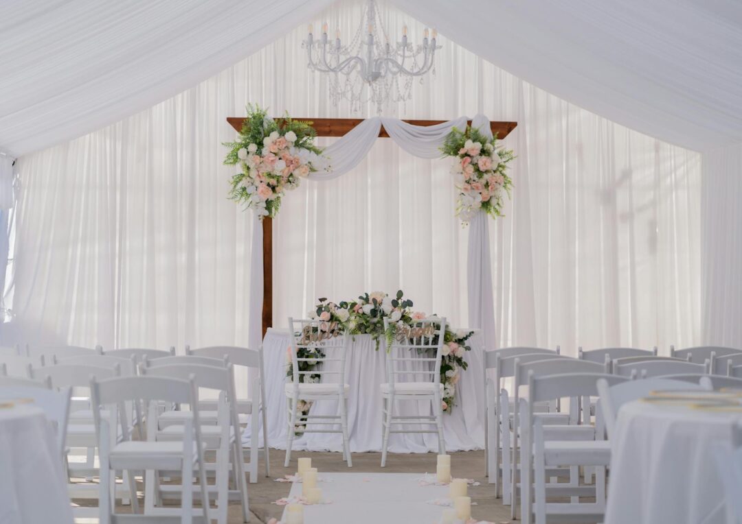 Minimalist wedding ceremony arch with soft white and green florals, couple standing close together, 15-20 guests gathered in a semi-circle a