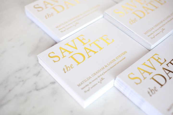 Stacks of Paperlust save the date cards with bold gold foil typography