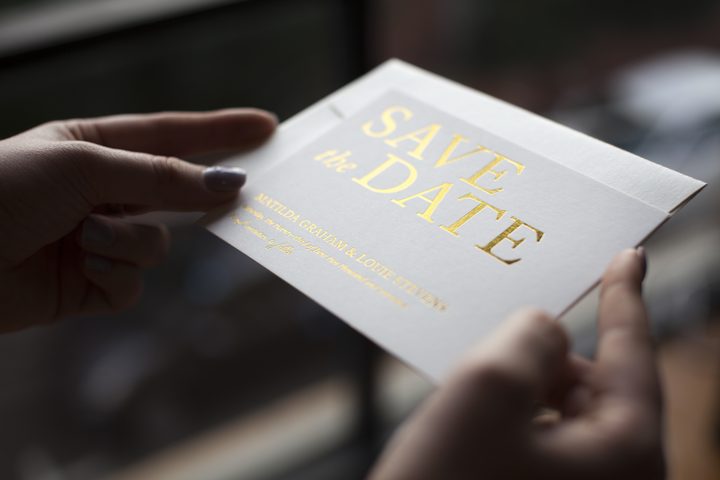 Hands holding a Paperlust landscape save the date card with gold foil typography wording