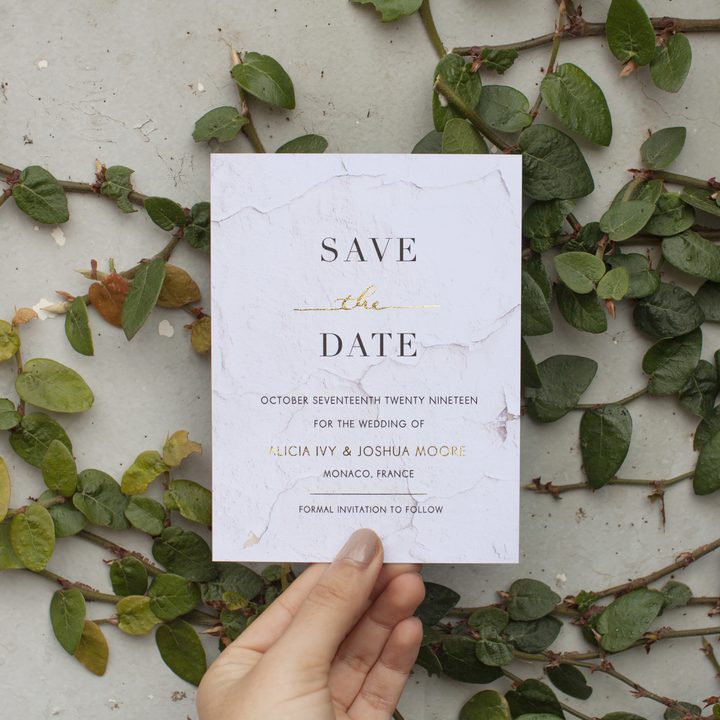 Hand holding a Paperlust marble-textured save the date card with gold foil typography
