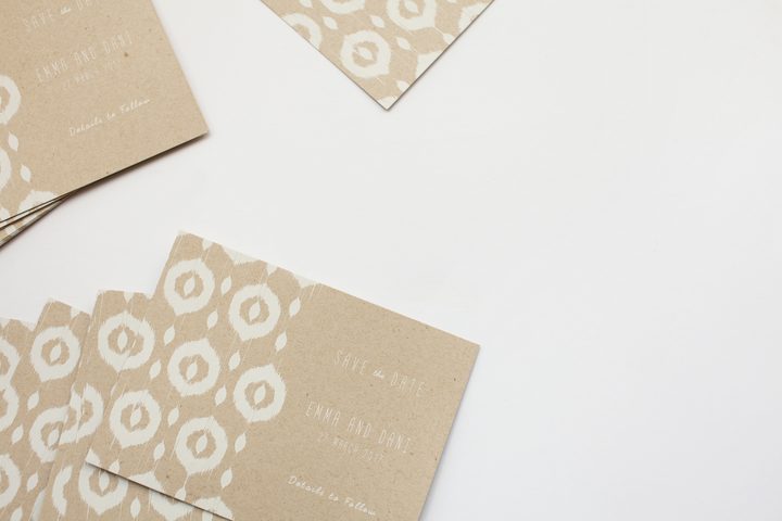 Multiple Paperlust kraft paper save the date cards with ikat pattern in white awaiting addressing