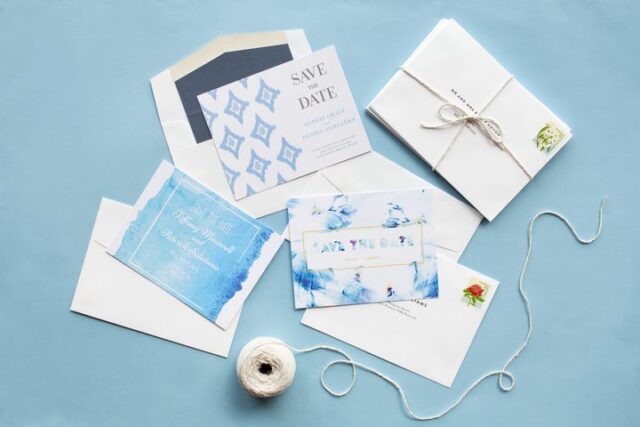 Paperlust flatlay of multiple save the date card designs in blue and white watercolour with envelopes and stamps for addressing