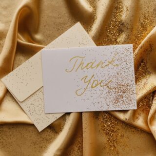 Paperlust thank you card flatlay -- elegant cream card with gold foil text on a linen surface, envelope alongside, soft natural light