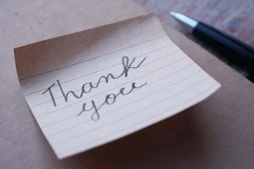 Paperlust thank you card close-up, handwritten note inside an opened printed card, warm natural light, styled on a wooden desk with a pen