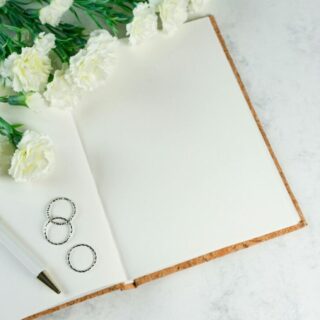 Paperlust wedding invitation flatlay with planner notebook, pen, and white envelope on a marble surface - overhead editorial shot