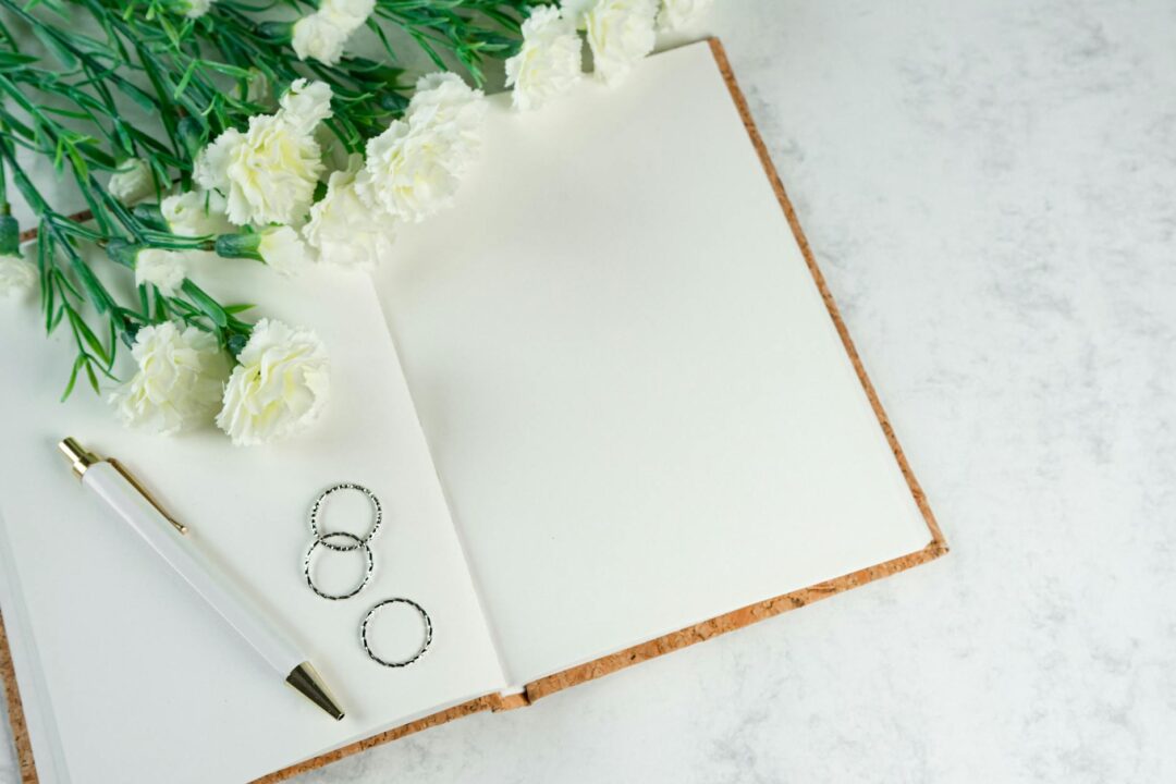 Paperlust wedding invitation flatlay with planner notebook, pen, and white envelope on a marble surface - overhead editorial shot