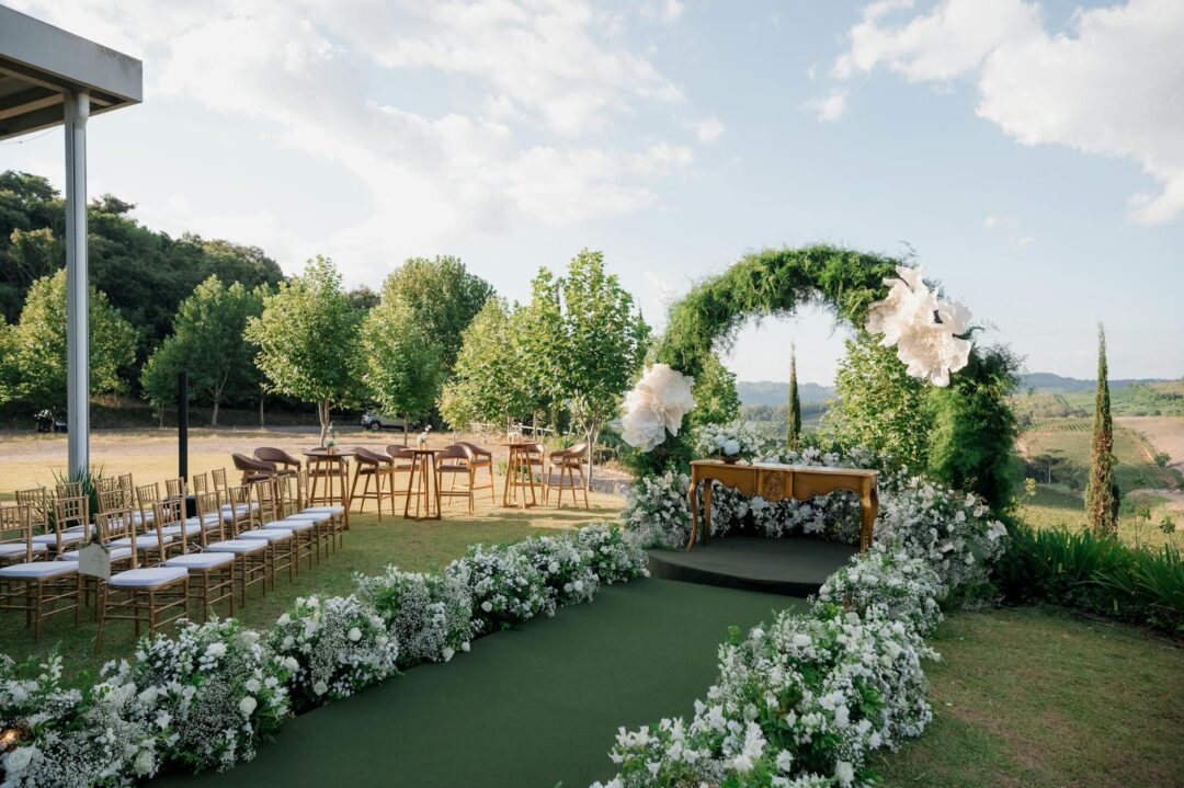 wide-angle outdoor wedding ceremony aisle lined with white florals and greenery, soft natural light, romantic garden or barn setting