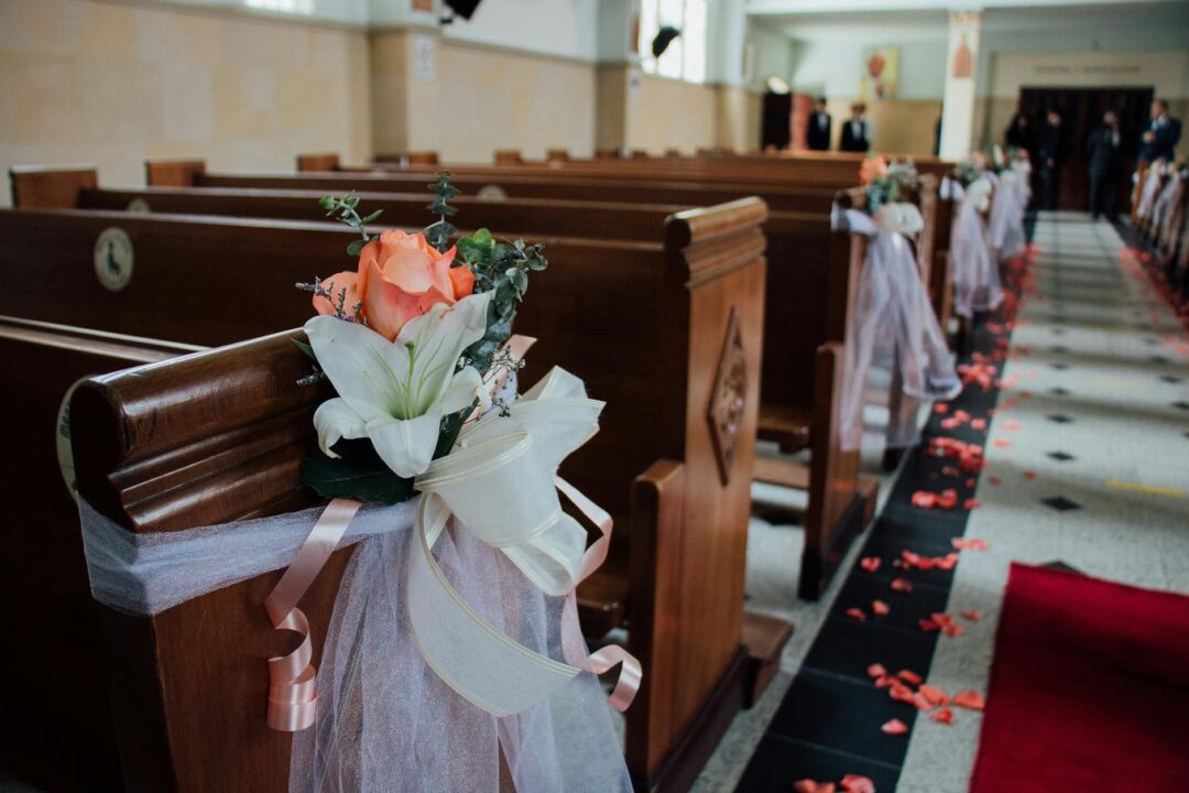 close-up of white and greenery pew-end florals on wooden church pews with soft window light