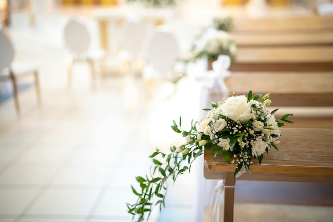 elegant ballroom wedding ceremony aisle with tall floral pedestal arrangements, velvet runner, white ribbon chair ties, warm chandelier ligh