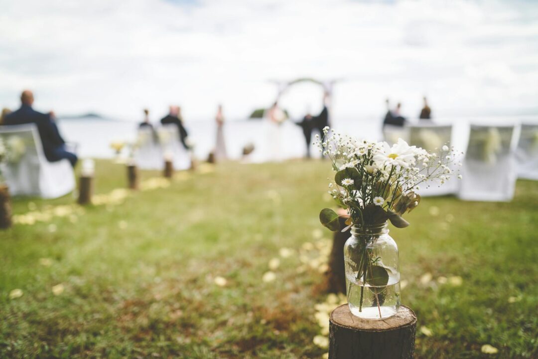 DIY barn wedding aisle with mason jar wildflower arrangements on shepherd's hooks, string lights overhead, burlap and lace chair ties, warm