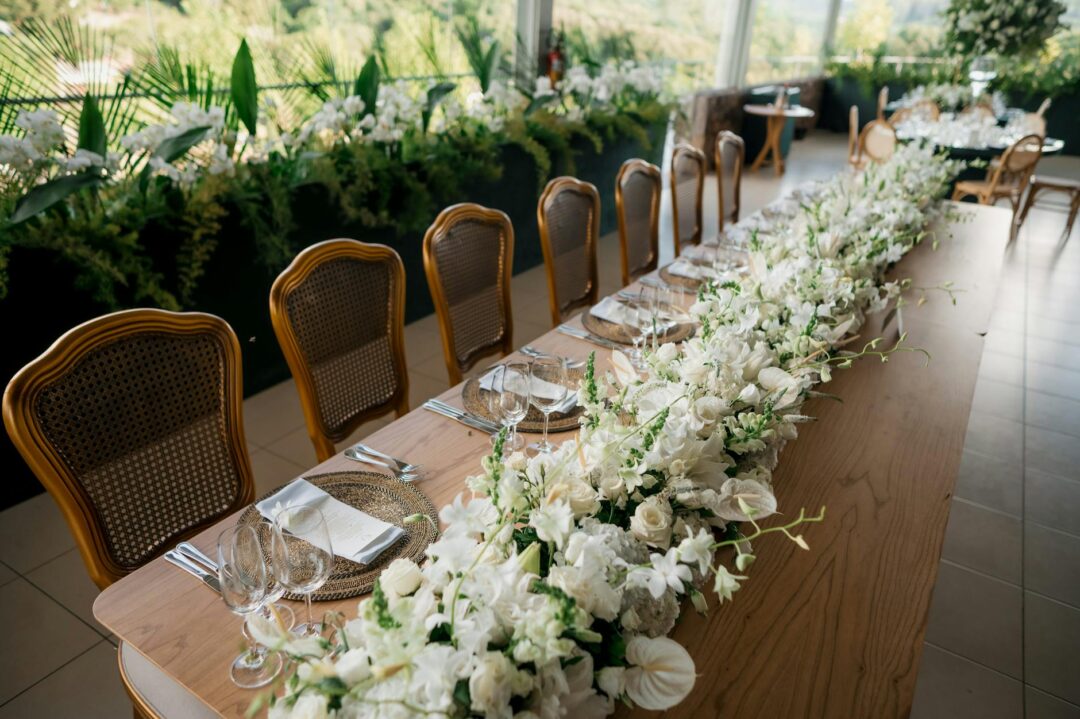 romantic wedding reception long table decorated with ceremony florals repurposed as centerpieces, candles, and greenery garland along the ta