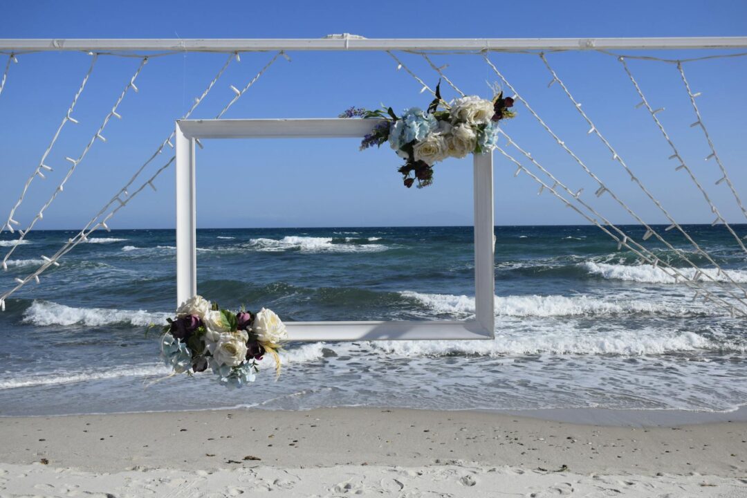 beach wedding arch with driftwood frame, tropical florals and orchids, ocean backdrop, daytime ceremony