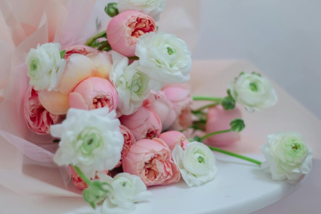 close-up of a lush bridal bouquet featuring garden roses, ranunculus, and eucalyptus in soft blush and ivory tones, held by a bride in a white gown