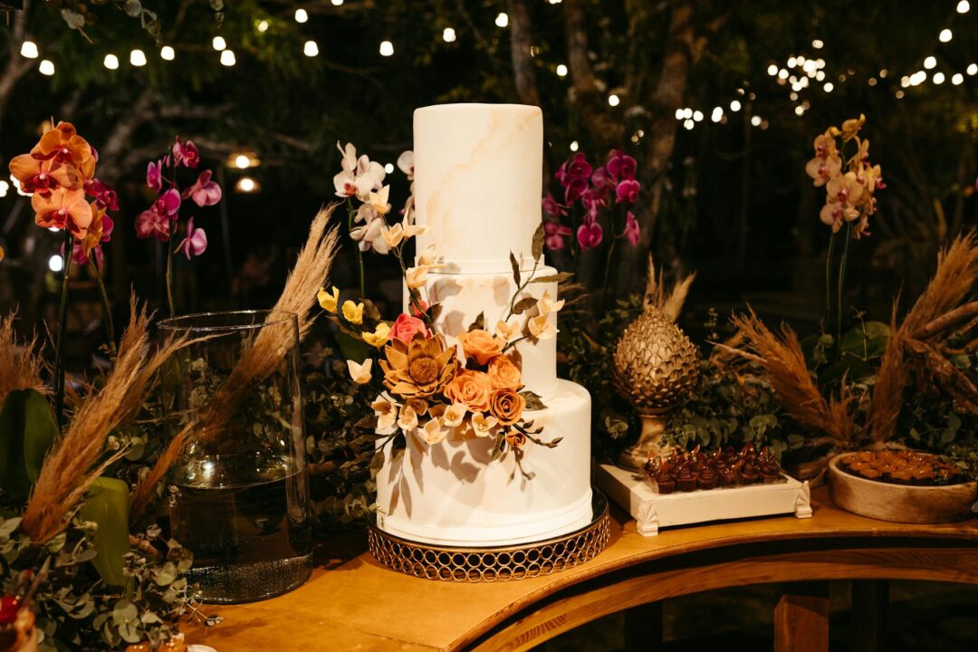 modern 2026 wedding cake display, cluster of mini cakes at varying heights on marble risers, white buttercream with pressed flowers and meta