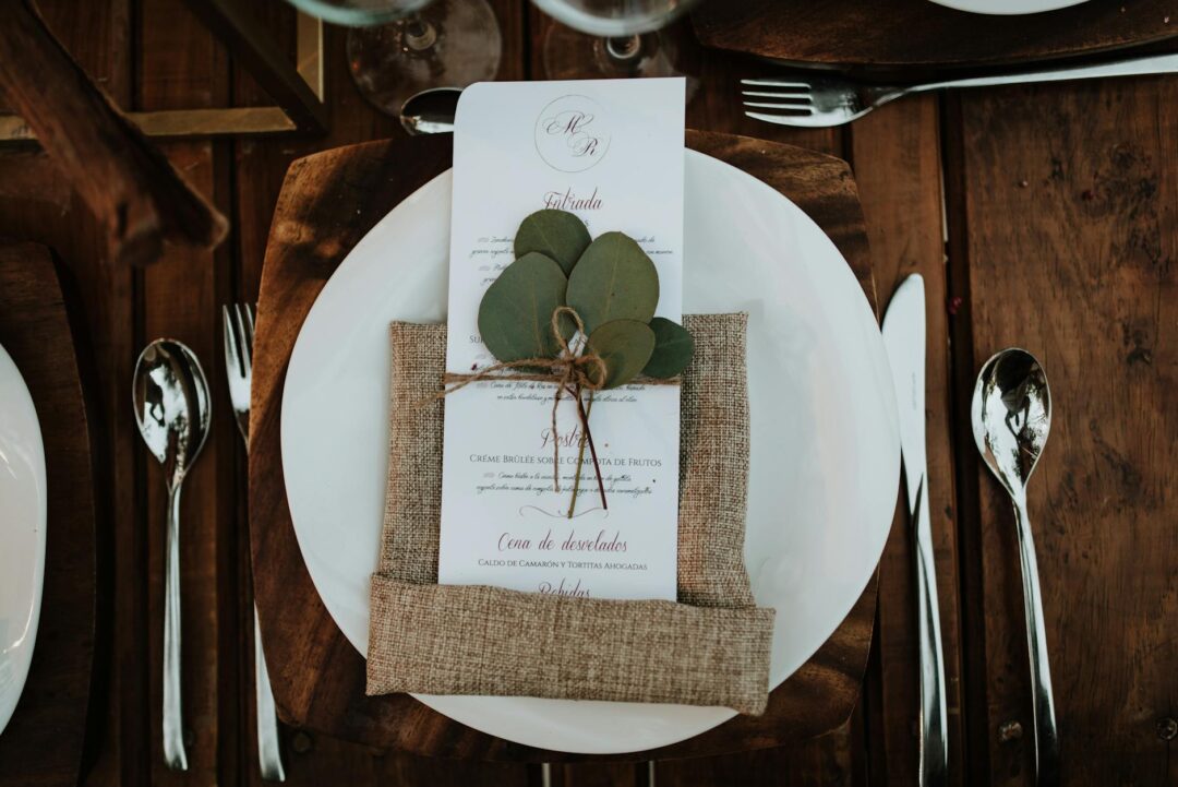 close-up of wedding menus printed on cream card stock with gold foil typography, fanned out on a white tablecloth alongside a floral arrange