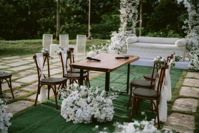 Wedding ceremony table setup with flowers, candles, and stationery including an order-of-service program.