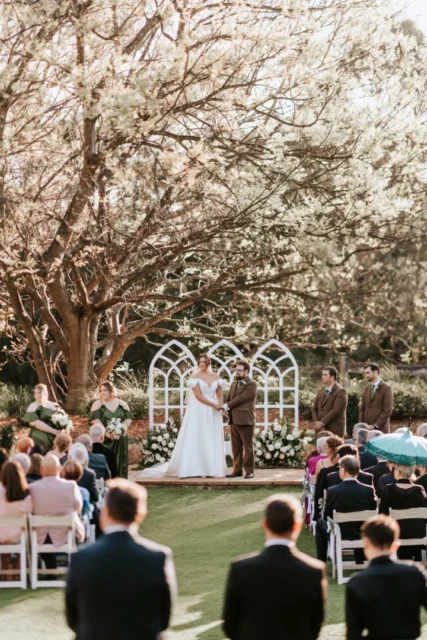 Bride and groom at outdoor wedding ceremony altar with gothic arch backdrop, exchanging vows in a candid emotional moment