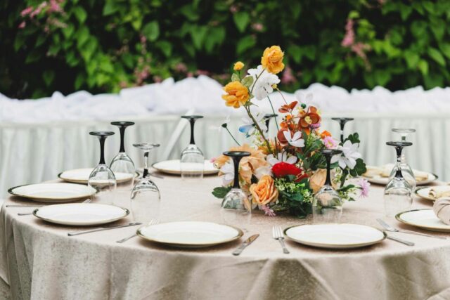 outdoor wedding cocktail hour, guests mingling with champagne flutes and craft cocktails, servers passing appetizers on silver trays, golden