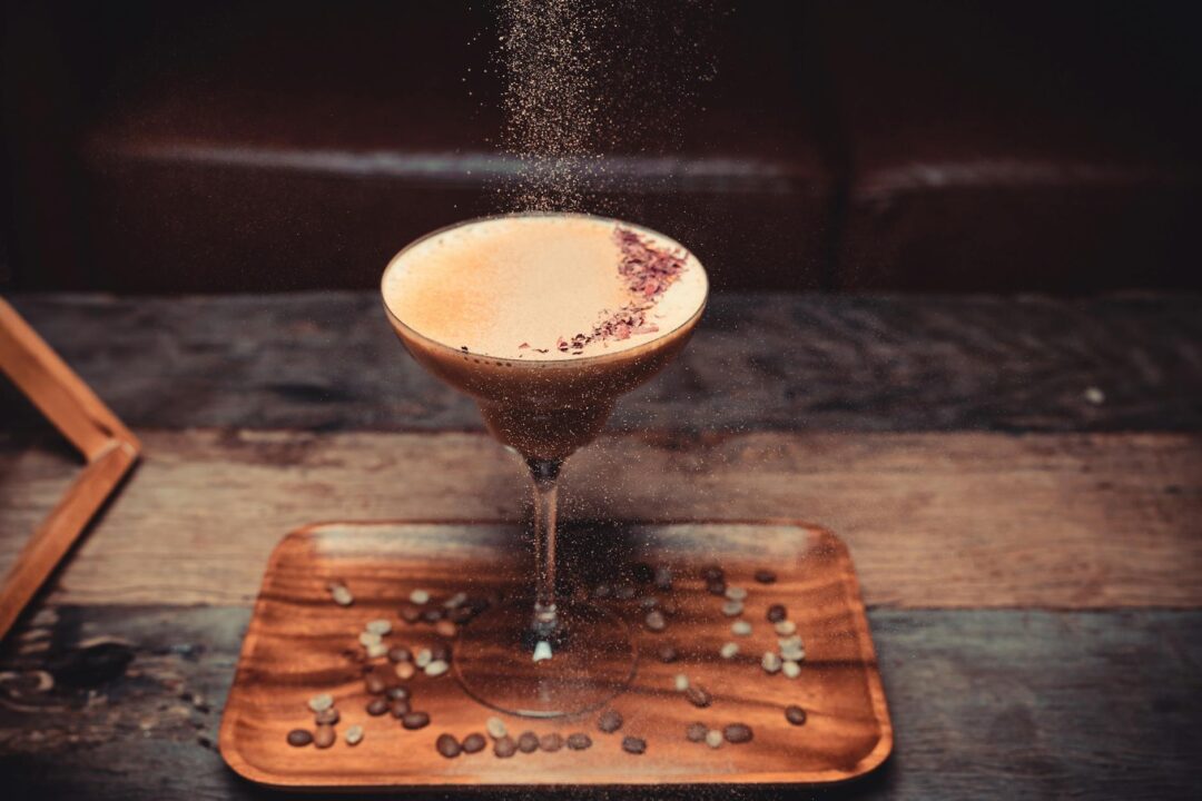 close-up of a wedding espresso martini cart with a barista in a white shirt preparing drinks, coffee beans, garnishes, and guests waiting wi