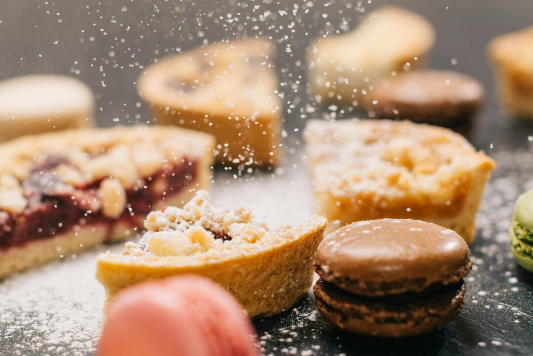 guest reaching for a mini macaron at a styled wedding dessert table, gold stands, soft florals in background