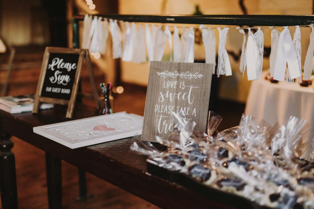 wedding favor table with a handwritten chalkboard sign reading 'Please take a sweet treat home' surrounded by small kraft boxes and personal