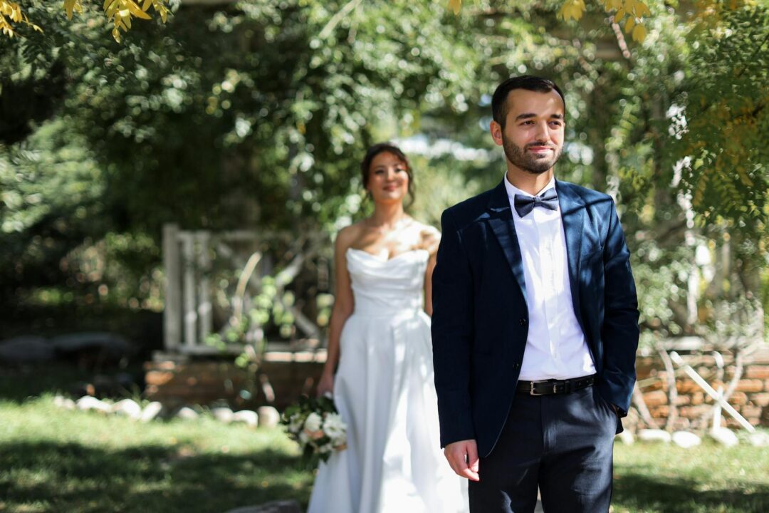 Bride and groom in a sunny outdoor setting, perfect for wedding bliss.'s back, bride approaching in white gown, soft natural light filtering through trees