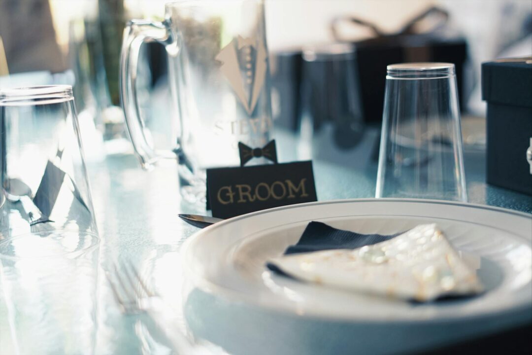 Elegant wedding reception table setting with printed menus alongside cutlery, white floral centerpiece and candlelight