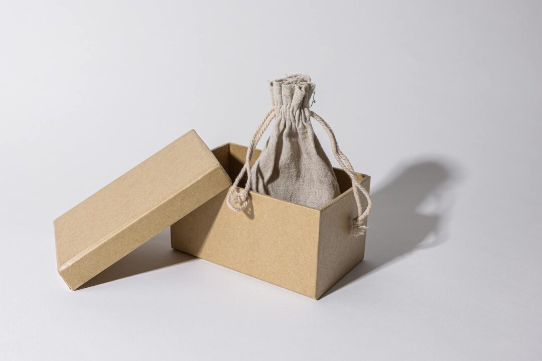 Open kraft paper gift bag with minimalist thank you tag featuring couple's monogram and dried wheat accent, wedding favor styling in warm ea